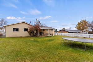 Rear view of property featuring a yard, a patio, and a trampoline