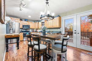 Dining space with french doors, light wood-type flooring, a textured ceiling, and a notable chandelier