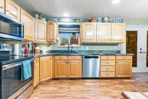 Kitchen with appliances with stainless steel finishes, a textured ceiling, light hardwood / wood-style flooring, and sink