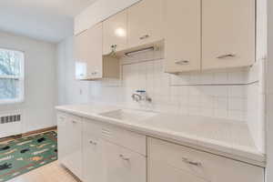 Kitchen with backsplash, light tile patterned flooring, sink, and radiator