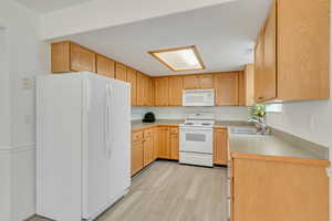 Kitchen featuring sink, light hardwood / wood-style floors, white appliances, and light brown cabinets