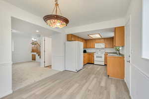 Kitchen with pendant lighting, white appliances, light hardwood / wood-style flooring, and sink