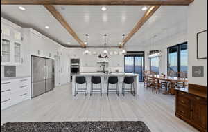 Kitchen featuring beam ceiling, stainless steel appliances, white cabinetry, and decorative light fixtures