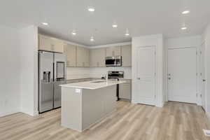 Kitchen featuring sink, an island with sink, light hardwood / wood-style floors, gray cabinets, and appliances with stainless steel finishes. Tech savy window fridge!