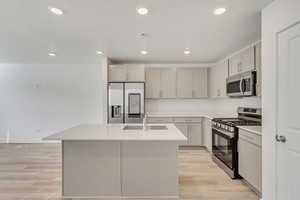 Kitchen island with sink, stainless steel appliances, quartz countertops, Tech glass door fridge, light hardwood / wood-style flooring.