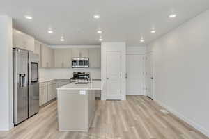 Kitchen with gray cabinetry, sink, light hardwood / wood-style flooring, an island with sink, and stainless steel appliances