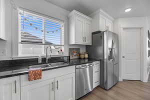 Kitchen featuring dark stone counters, white cabinets, sink, light wood-type flooring, and appliances with stainless steel finishes