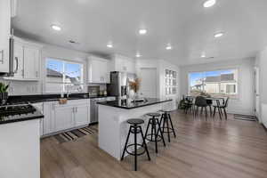 Kitchen featuring a kitchen bar, appliances with stainless steel finishes, white cabinets, hardwood / wood-style floors, and a center island