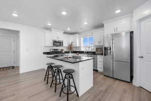 Kitchen with appliances with stainless steel finishes, light hardwood / wood-style flooring, white cabinetry, and a kitchen breakfast bar