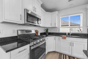 Kitchen featuring appliances with stainless steel finishes, sink, light hardwood / wood-style flooring, dark stone countertops, and white cabinets