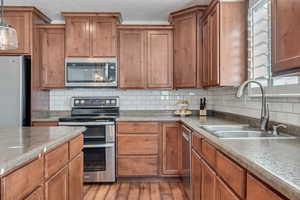 Kitchen featuring sink, hardwood / wood-style flooring, tasteful backsplash, decorative light fixtures, and stainless steel appliances