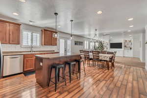 Kitchen featuring dishwasher, sink, light wood-type flooring, decorative light fixtures, and a kitchen island