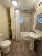 Bathroom with toilet, shower / bath combo with shower curtain, a textured ceiling, and a wealth of natural light