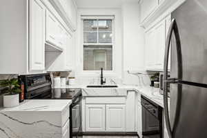 Kitchen with black appliances, light stone countertops, white cabinetry, and sink