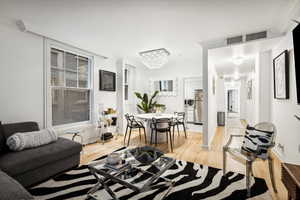 Living room with light wood-type flooring, ornamental molding, and a notable chandelier