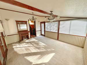 Unfurnished living room featuring a textured ceiling, lofted ceiling with beams, light colored carpet, and ceiling fan with notable chandelier