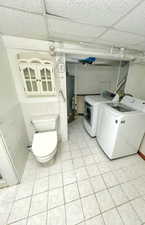 Clothes washing area featuring washer and clothes dryer, gas water heater, and light tile patterned floors