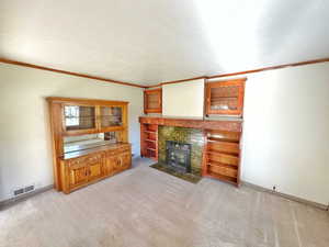 Unfurnished living room featuring a tile fireplace, crown molding, and light colored carpet