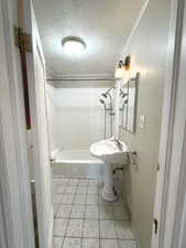 Bathroom featuring tile patterned flooring, tiled shower / bath combo, ornamental molding, and a textured ceiling