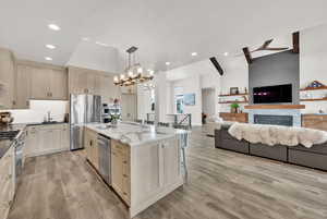 Kitchen featuring hanging light fixtures, a fireplace, appliances with stainless steel finishes, an island with sink, and light hardwood / wood-style floors