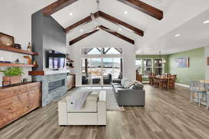 Living room featuring high vaulted ceiling, ceiling fan with notable chandelier, light hardwood / wood-style flooring, a fireplace, and beam ceiling