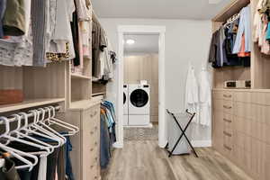 Walk in closet with independent washer and dryer and light hardwood / wood-style flooring