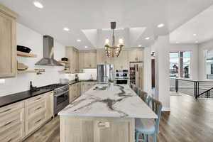 Kitchen with a breakfast bar, appliances with stainless steel finishes, a center island with sink, and exhaust hood