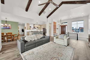 Living room with lofted ceiling with beams, light hardwood / wood-style floors, and ceiling fan with notable chandelier