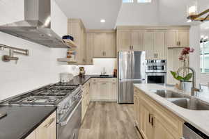 Kitchen featuring sink, wall chimney exhaust hood, backsplash, light hardwood / wood-style floors, and appliances with stainless steel finishes