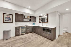 Kitchen featuring dark brown cabinetry, sink, stainless steel microwave, beverage cooler, and light wood-type flooring