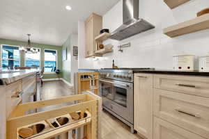 Kitchen featuring stainless steel range, ventilation hood, a chandelier, light brown cabinetry, and light wood-type flooring