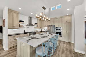 Kitchen with sink, hanging light fixtures, stainless steel appliances, wall chimney range hood, and light hardwood / wood-style floors