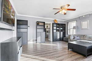 Living room featuring laminate flooring, ceiling fan, and ornamental molding