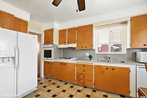 Kitchen with decorative backsplash, white appliances, ceiling fan, and sink