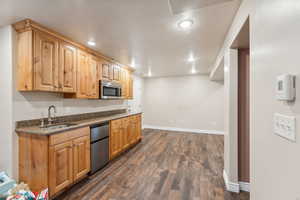 Kitchen with dishwasher, dark stone counters, dark wood-type flooring, and sink