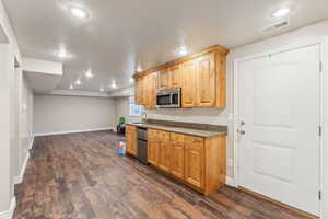 Kitchen with a textured ceiling, sink, light brown cabinetry, and dark wood-type flooring