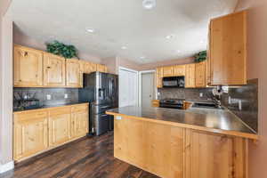 Kitchen with sink, dark wood-type flooring, tasteful backsplash, kitchen peninsula, and black appliances