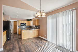 Kitchen with dark wood-type flooring, a chandelier, decorative light fixtures, decorative backsplash, and black appliances