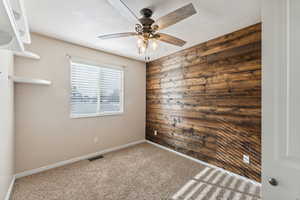 Carpeted spare room featuring ceiling fan, a textured ceiling, and wooden walls