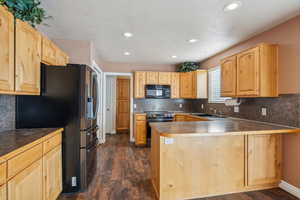 Kitchen with kitchen peninsula, black appliances, and dark hardwood / wood-style floors