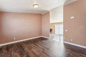 Empty room with dark hardwood / wood-style floors and vaulted ceiling