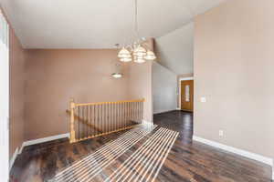 Hall with dark hardwood / wood-style flooring, an inviting chandelier, and lofted ceiling