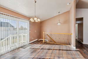 Spare room with dark hardwood / wood-style floors, an inviting chandelier, a textured ceiling, and vaulted ceiling