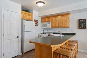 Kitchen featuring sink, a kitchen breakfast bar, kitchen peninsula, a textured ceiling, and white appliances