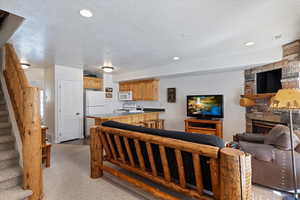 Carpeted living room with sink, a stone fireplace, and a textured ceiling