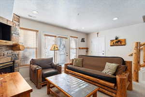 Carpeted living room featuring a stone fireplace and a textured ceiling