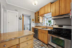 Kitchen with light stone countertops, ornamental molding, sink, and appliances with stainless steel finishes