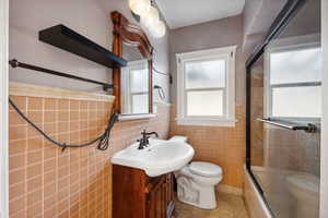 Full bathroom featuring combined bath / shower with glass door, tile patterned floors, vanity, tile walls, and toilet