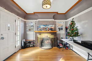 Entrance foyer with wood-type flooring, a brick fireplace, a wealth of natural light, and crown molding