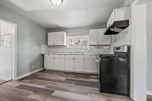 Kitchen featuring white cabinetry, stainless steel gas range, ventilation hood, tasteful backsplash, and dark wood-type flooring